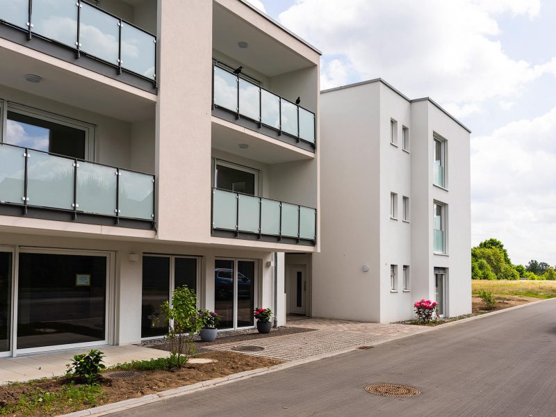 Barrierefreier Zugang zur Seniorenwohnanlage mit bepflanzten Kübeln und bodentiefen Fenstern.