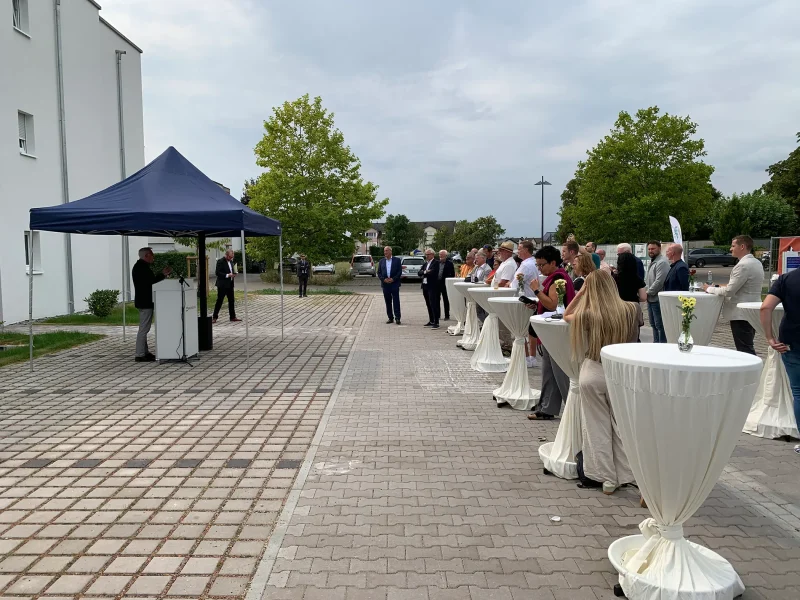 Zwei Teilnehmer im Gespräch vor dem Banner der orbau Firmengruppe bei der Glasfaser-Feier in Kirrlach.