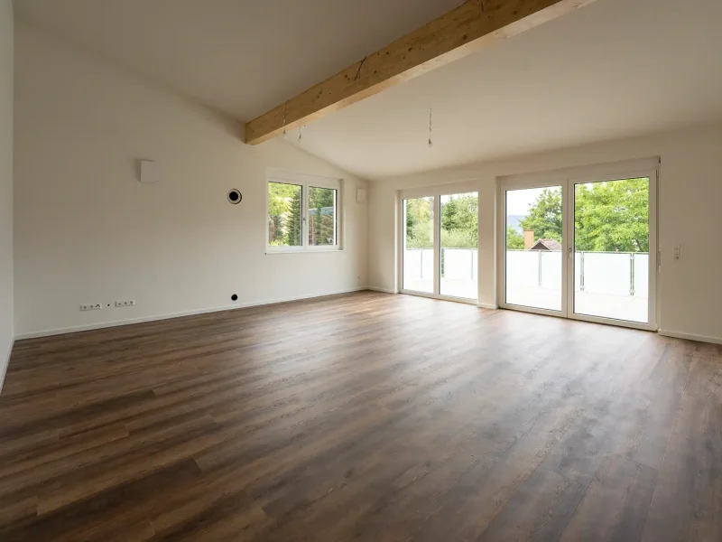 Heller Wohnbereich mit Holzboden, sichtbarem Deckenbalken und großen Fenstern