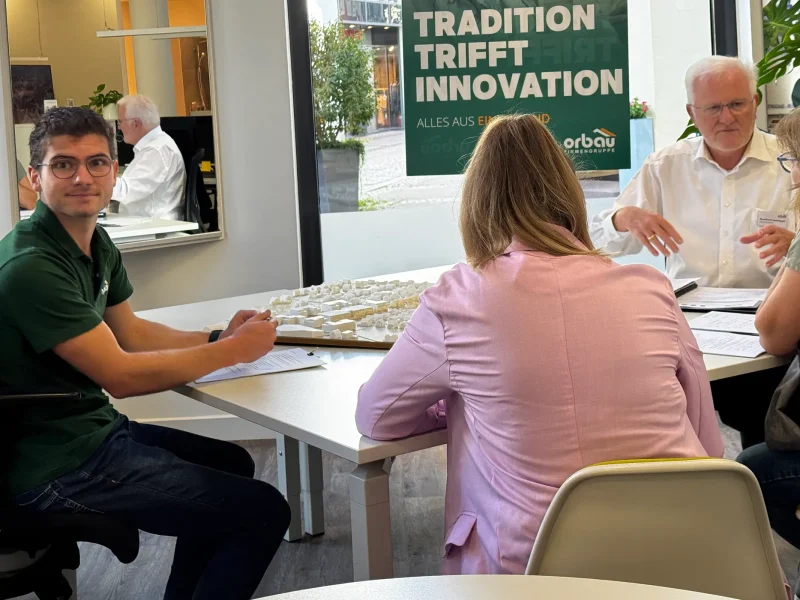 Beratungsgespräch am Tisch mit Modell des Neubauprojekts Fessenbach im orbau Büro