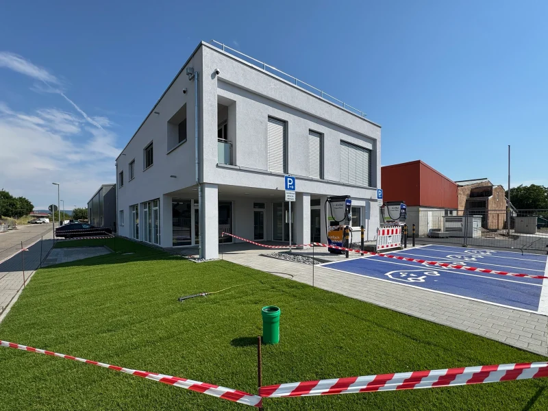 Blick auf das Bürogebäude mit Rasenfläche, markierten E-Parkplätzen und Ladeinfrastruktur.